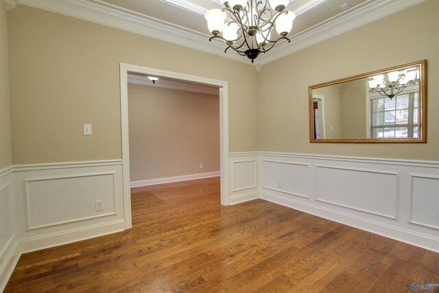 empty room with wainscoting, wood finished floors, ornamental molding, and a chandelier
