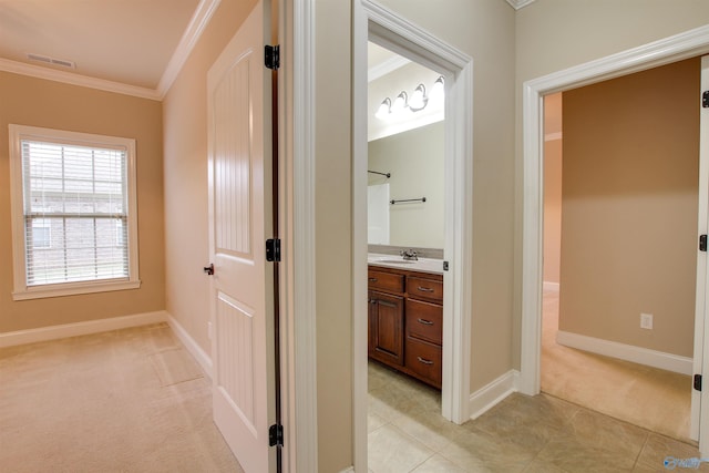 corridor featuring crown molding, baseboards, a sink, visible vents, and light carpet