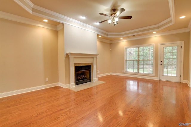 unfurnished living room with a fireplace with flush hearth, a tray ceiling, a ceiling fan, and light wood finished floors