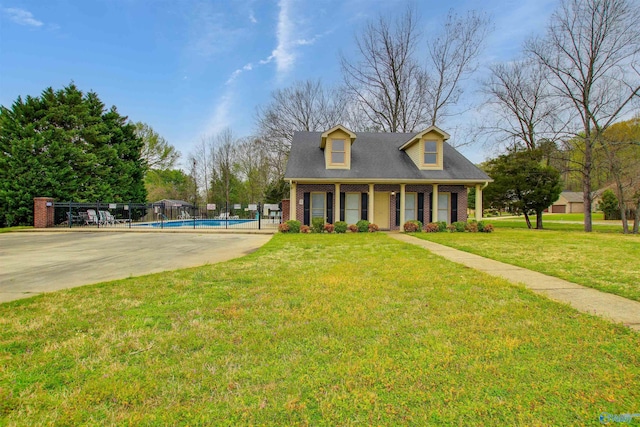 cape cod home featuring fence, a fenced in pool, concrete driveway, a front yard, and brick siding