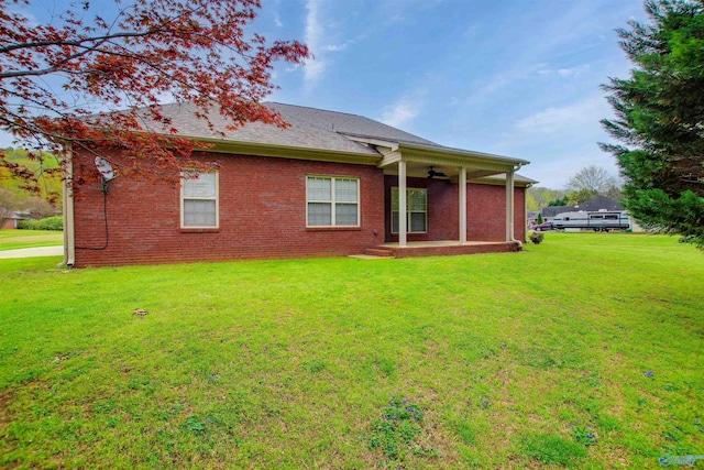 back of house featuring roof with shingles, brick siding, a yard, and ceiling fan