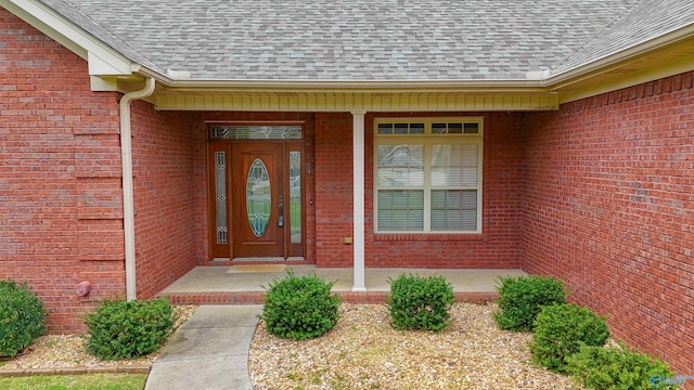view of exterior entry with brick siding and roof with shingles