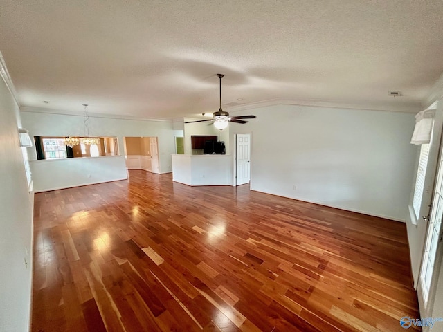 unfurnished living room with ceiling fan with notable chandelier, a textured ceiling, hardwood / wood-style flooring, and crown molding