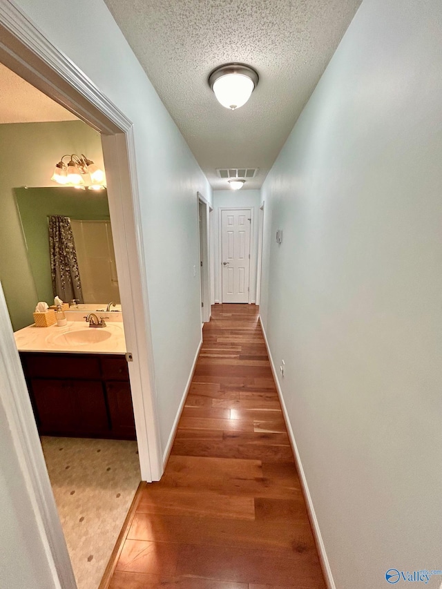 hallway with a textured ceiling, wood-type flooring, and sink