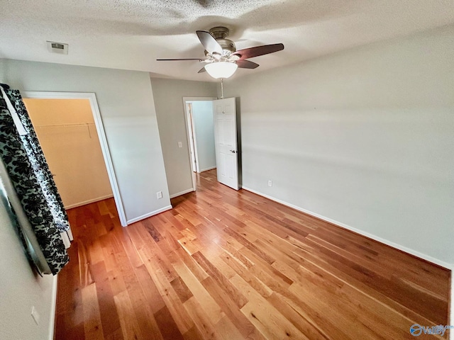 unfurnished bedroom with ceiling fan, a spacious closet, a textured ceiling, light hardwood / wood-style floors, and a closet