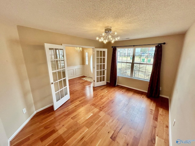 unfurnished room with hardwood / wood-style floors, french doors, a chandelier, and a textured ceiling