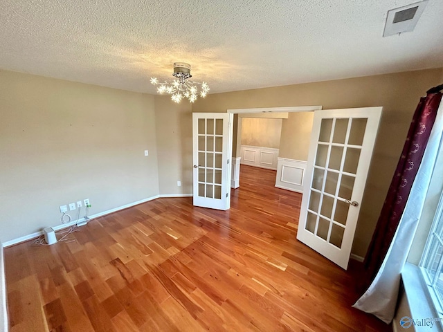 spare room featuring a chandelier, french doors, a textured ceiling, and hardwood / wood-style floors