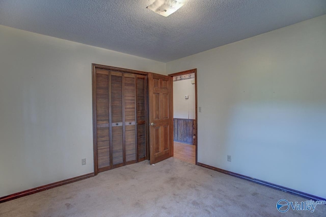 unfurnished bedroom featuring light carpet, a closet, a textured ceiling, and baseboards