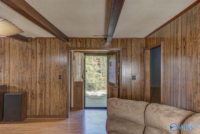 unfurnished living room with light wood-type flooring, wood walls, a textured ceiling, and beamed ceiling