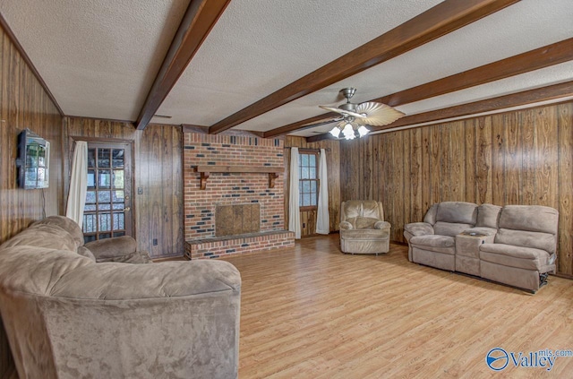 living area with a textured ceiling, light wood-style flooring, wooden walls, a fireplace, and beamed ceiling