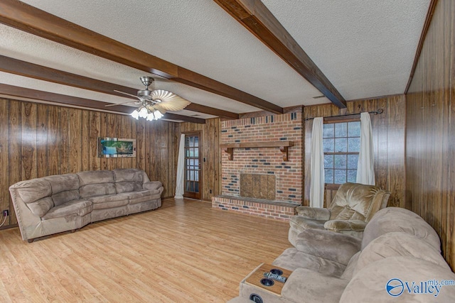 living room featuring wooden walls, beamed ceiling, a textured ceiling, light wood-style floors, and a fireplace