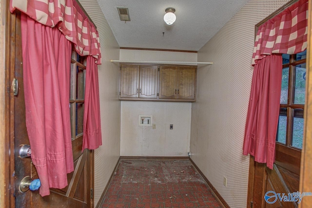 laundry area featuring cabinet space, wallpapered walls, hookup for a washing machine, brick floor, and a textured ceiling