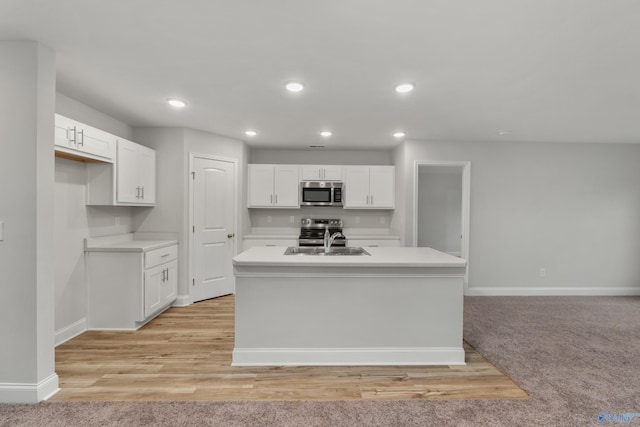 kitchen with sink, a kitchen island with sink, white cabinetry, stainless steel appliances, and light hardwood / wood-style floors