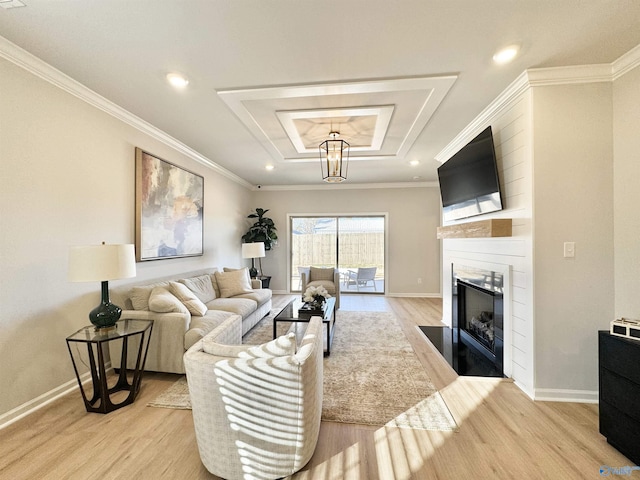 living area featuring a large fireplace, baseboards, a tray ceiling, ornamental molding, and light wood-style flooring