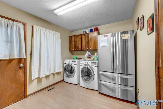 clothes washing area with washing machine and dryer, a textured ceiling, and light hardwood / wood-style flooring