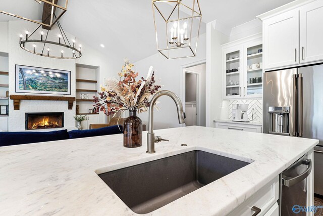 kitchen featuring light stone countertops, a sink, a chandelier, high end refrigerator, and glass insert cabinets