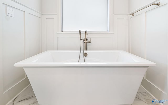full bath featuring marble finish floor, a decorative wall, and a freestanding bath