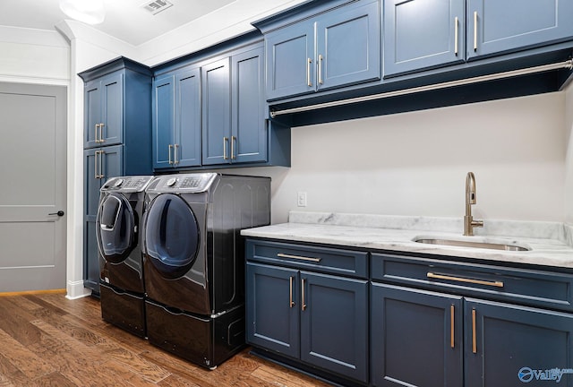laundry room with visible vents, washing machine and clothes dryer, cabinet space, a sink, and dark wood-style floors