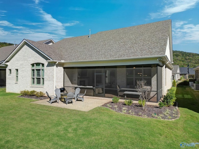 rear view of property featuring a sunroom, a shingled roof, a patio area, and a lawn