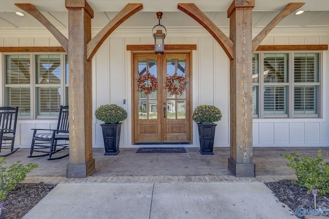 view of exterior entry featuring board and batten siding, french doors, and covered porch