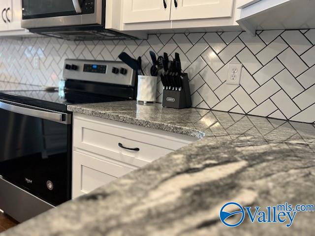 kitchen featuring tasteful backsplash, white cabinetry, light stone countertops, and appliances with stainless steel finishes