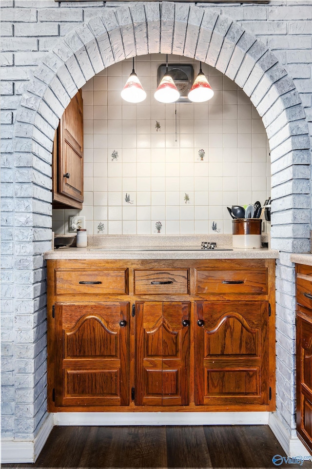 kitchen with brick wall, brown cabinets, dark wood-style flooring, decorative light fixtures, and light countertops