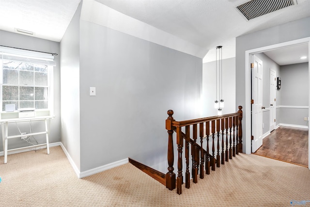 corridor with baseboards, visible vents, light colored carpet, and an upstairs landing