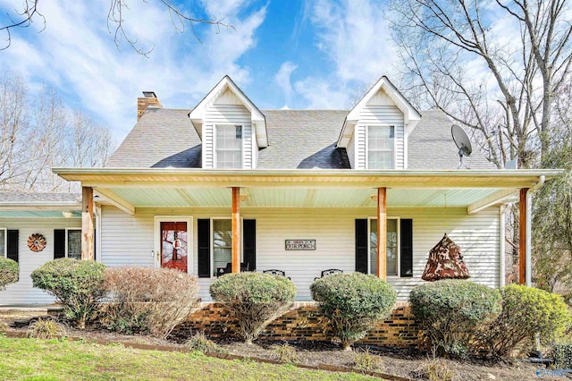 cape cod house with roof with shingles, a porch, and a chimney