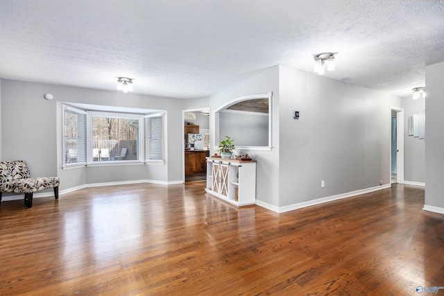 unfurnished living room featuring baseboards, dark wood finished floors, and a textured ceiling