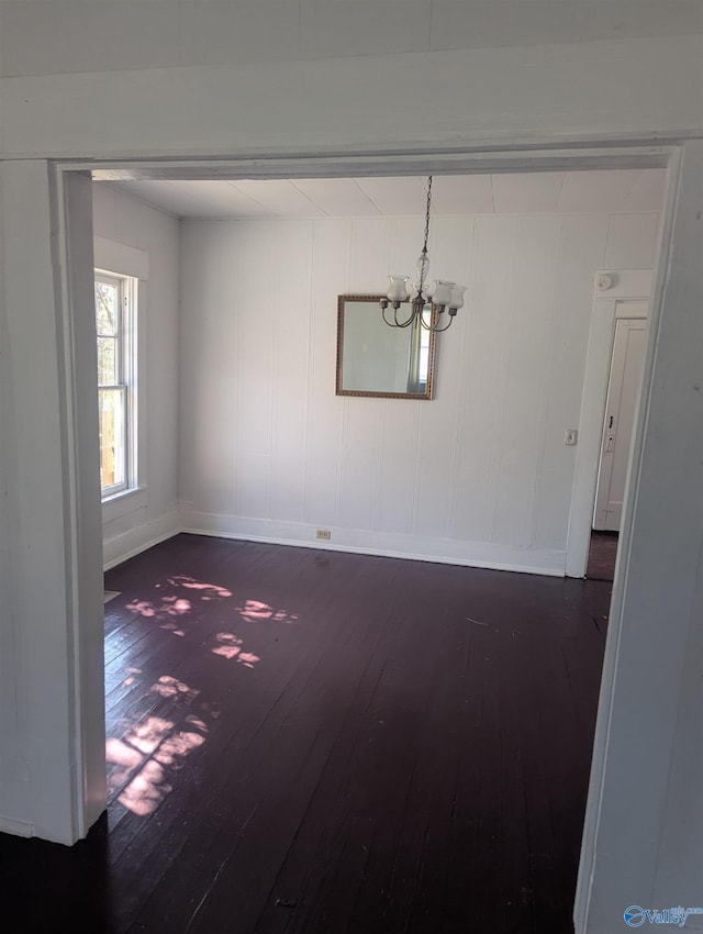 unfurnished room featuring baseboards, an inviting chandelier, and hardwood / wood-style flooring