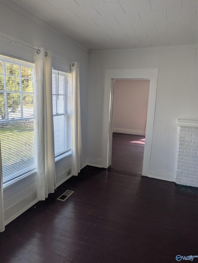 empty room featuring visible vents, dark wood-style floors, and ornamental molding