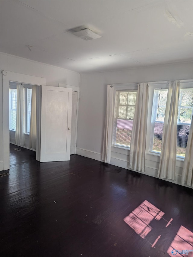 unfurnished room with dark wood finished floors, a healthy amount of sunlight, and baseboards