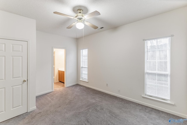 unfurnished bedroom with ceiling fan, light colored carpet, ensuite bath, and a textured ceiling