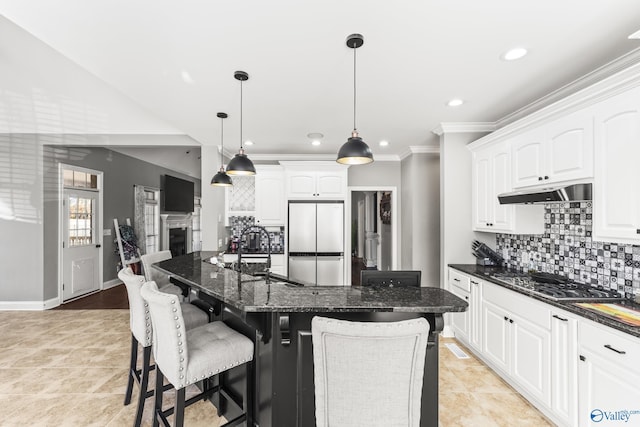 kitchen featuring a kitchen island, refrigerator, white cabinetry, dark stone countertops, and stainless steel gas cooktop