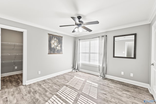 unfurnished bedroom featuring hardwood / wood-style floors, a walk in closet, ceiling fan, crown molding, and a closet