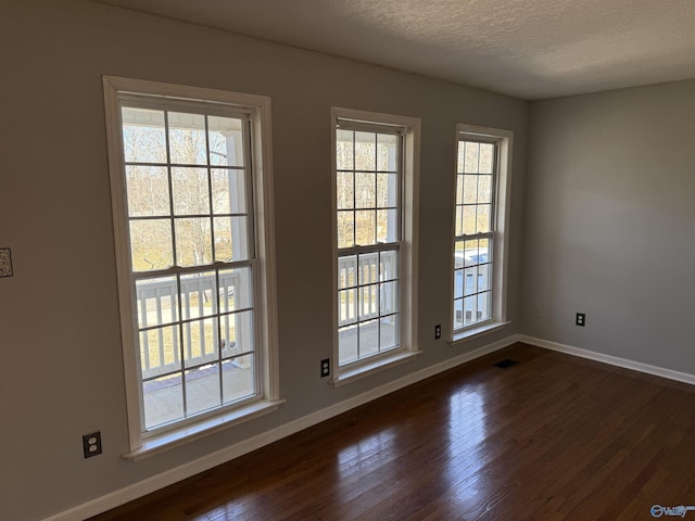 unfurnished room with baseboards, a textured ceiling, visible vents, and dark wood-type flooring