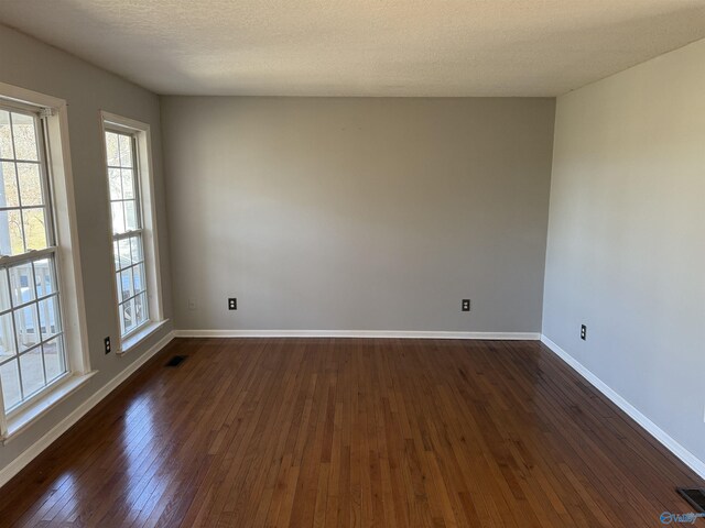 empty room with dark wood-style floors, visible vents, a textured ceiling, and baseboards