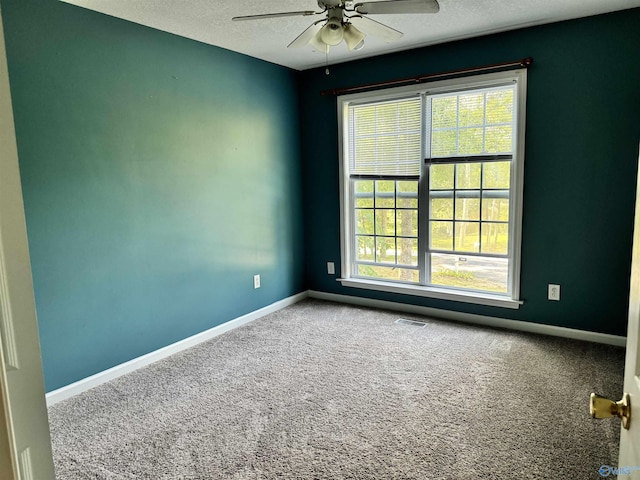 carpeted spare room featuring baseboards, ceiling fan, visible vents, and a healthy amount of sunlight