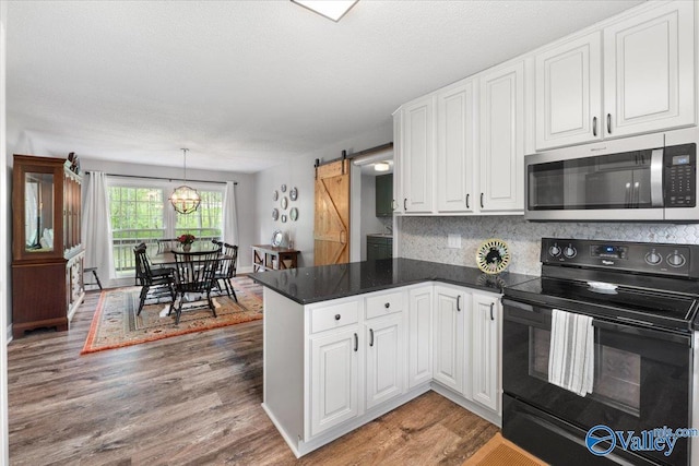 1762 Old Big Cove Rd SE, Owens Cross Roads, AL 35763 - kitchen featuring black range with electric cooktop, a barn door, a peninsula, stainless steel microwave, and white cabinetry