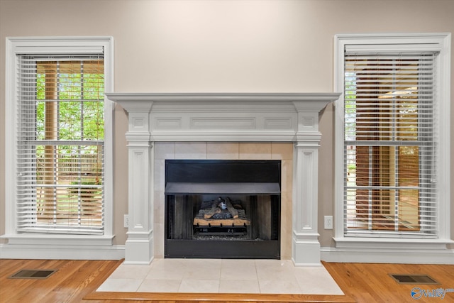details featuring baseboards, visible vents, a tiled fireplace, and wood finished floors
