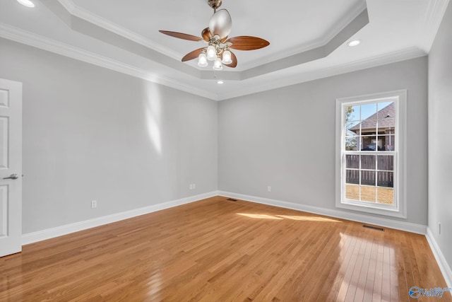 unfurnished room featuring ornamental molding, ceiling fan, light wood-type flooring, and a raised ceiling