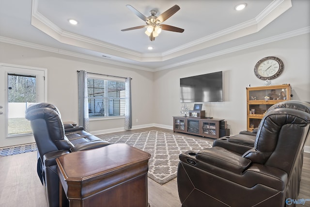 living room with a raised ceiling, ceiling fan, crown molding, and light wood-type flooring