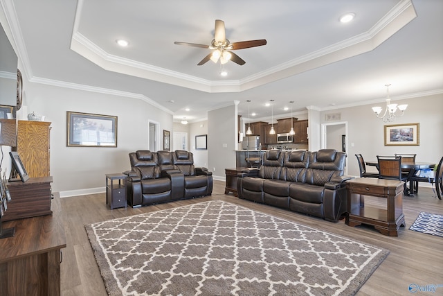 living room featuring wood-type flooring, ceiling fan with notable chandelier, crown molding, and a tray ceiling