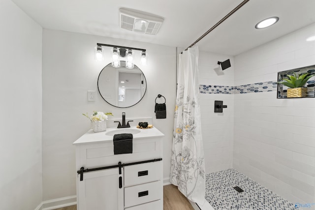 bathroom featuring wood finished floors, tiled shower, vanity, and visible vents