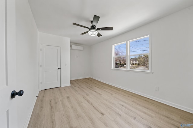 unfurnished bedroom with baseboards, a wall mounted air conditioner, a ceiling fan, and light wood-style floors