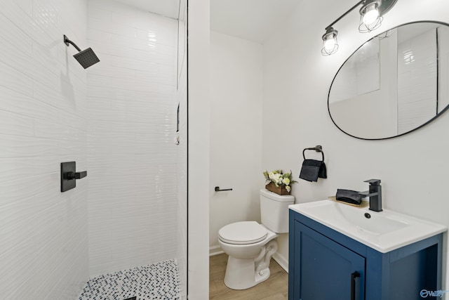 bathroom with toilet, wood finished floors, vanity, baseboards, and a tile shower