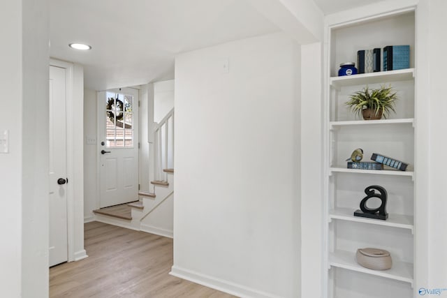 hallway featuring baseboards, stairs, built in features, and wood finished floors