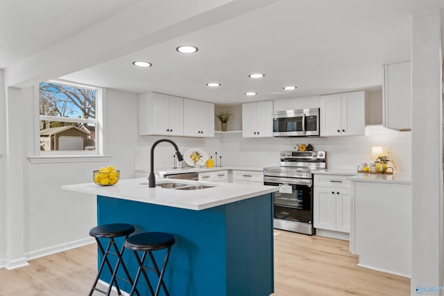 kitchen with light wood-style flooring, appliances with stainless steel finishes, a sink, a kitchen bar, and backsplash