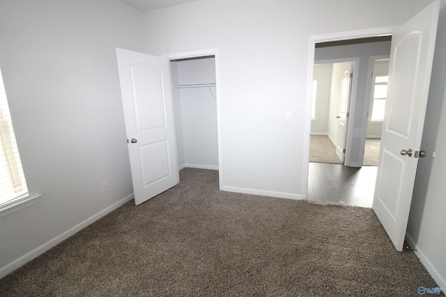 unfurnished bedroom featuring dark colored carpet, multiple windows, and a closet