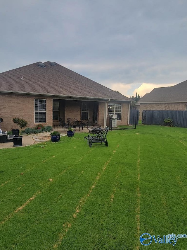 back of property at dusk with brick siding, a patio, fence, and a lawn